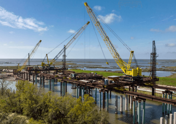 A construction site with large yellow cranes building a bridge over water
