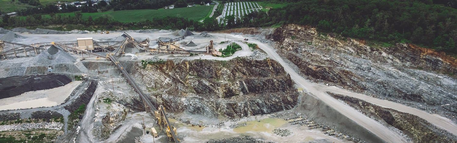 An open-pit quarry with machinery, conveyor belts, and piles of excavated material