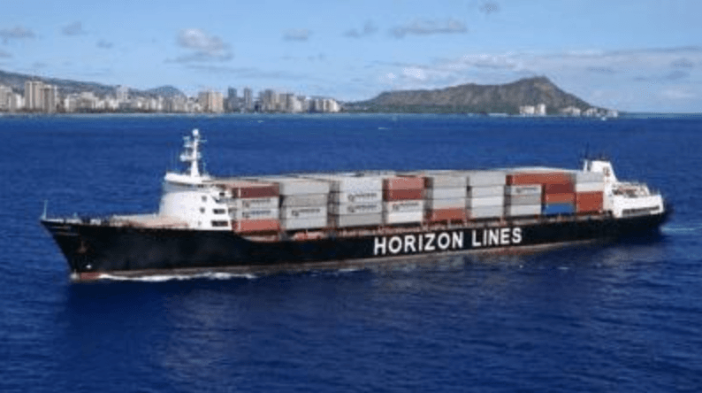 A cargo ship sailing with a city and mountain in the background