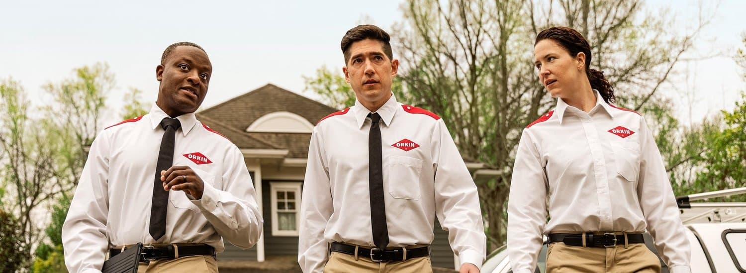 Three Orkin technicians in uniform standing outdoors in front of a house